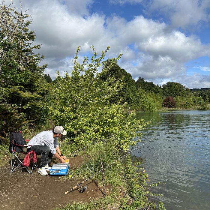 A man sits in a camp chair and attends two fishing poles on the Hagg Lake shoreline